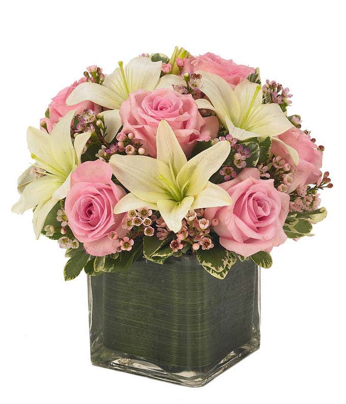 Light pink roses, white lilies and pink waxflower in square vase 