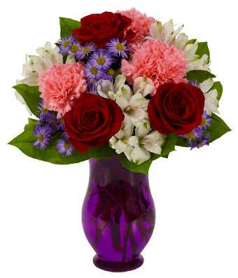 Red roses, pink carnations and white alstroemeria in a purple vase