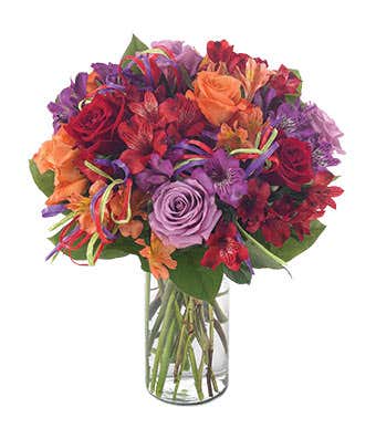 Purple roses, orange roses, red roses and alstroemeria in glass vase