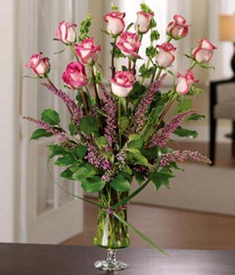 One dozen bi-color roses with seasonal greens in luxury vase