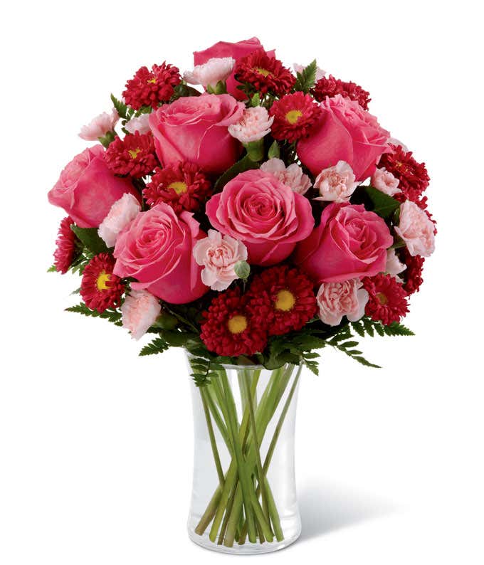 Pink roses, red asters, and light pink carnations arranged into a tall cylinder vase